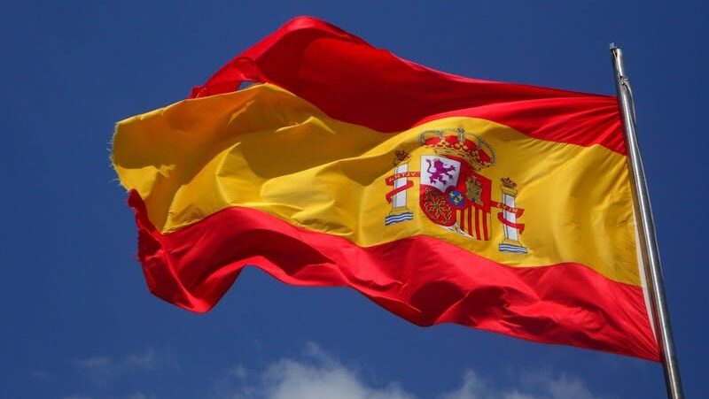 Vibrant Spanish flag waving against a clear blue sky and clouds.
