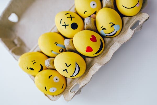 Bright yellow Easter eggs painted with emoji faces, arranged in a carton. Perfect for a festive and fun holiday theme.