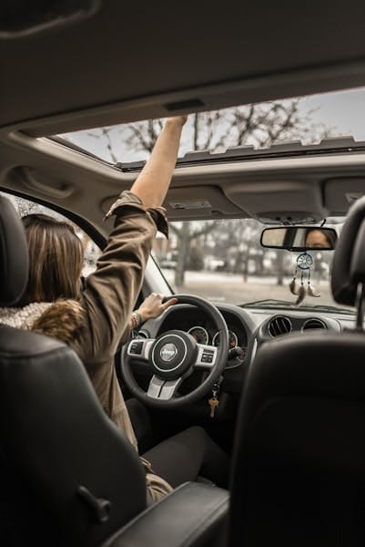A young woman enjoying a drive with the sunroof open, showing car interior detail.