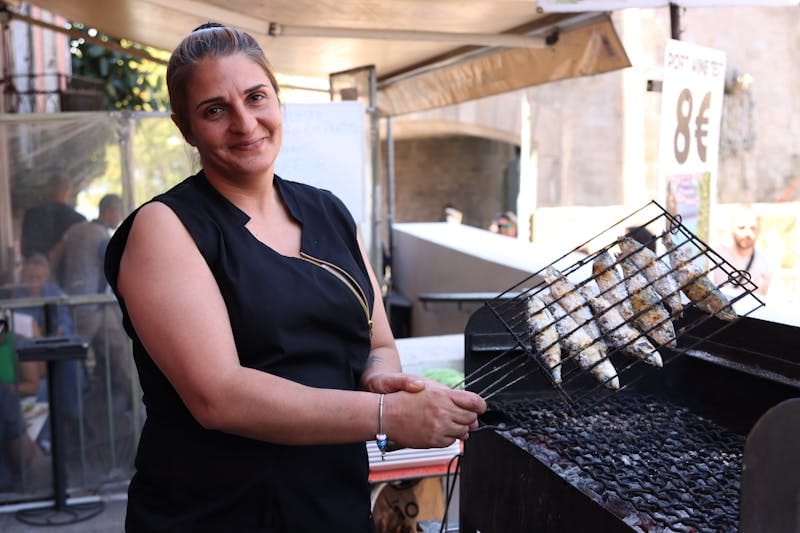A female chef grilling fish outdoors at a food stall in Porto, Portugal.