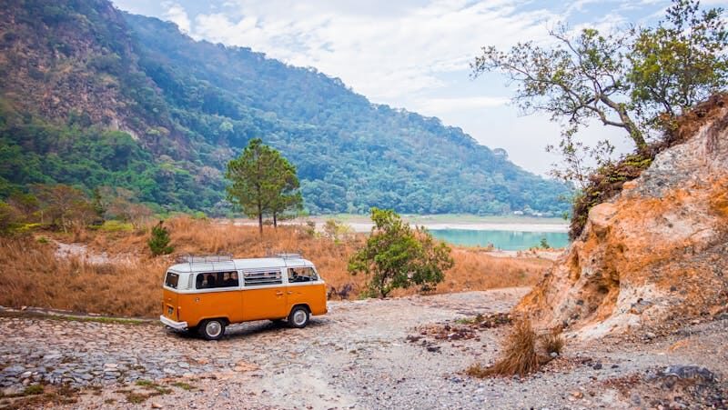 Explore El Salvador's natural beauty with a classic VW bus by a serene lakeside view.
