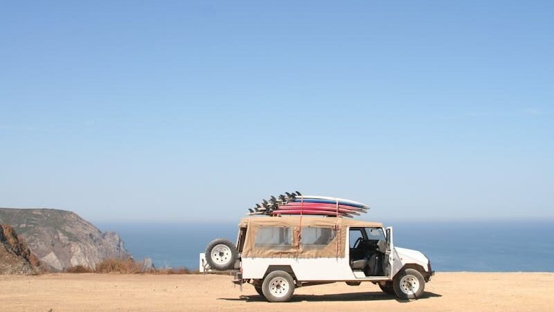 A jeep loaded with surfboards parked by a scenic ocean cliff under a clear sky.
