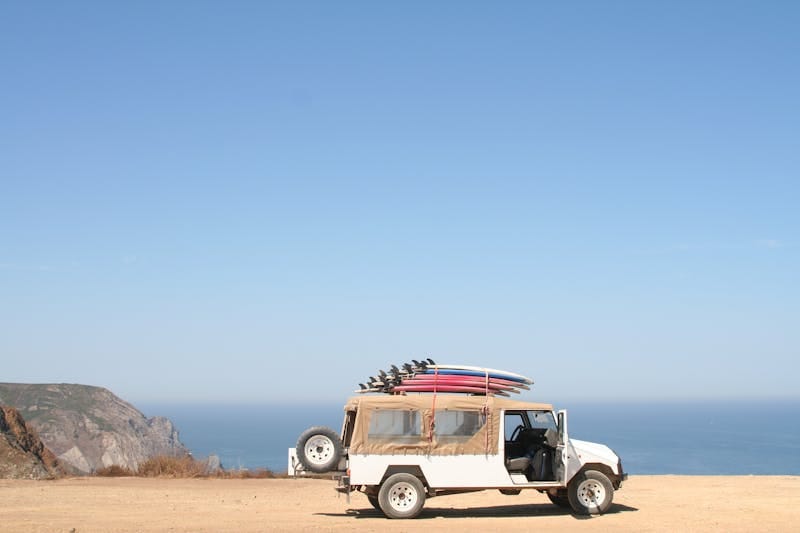 A jeep loaded with surfboards parked by a scenic ocean cliff under a clear sky.