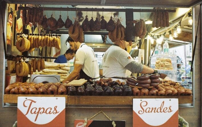 A vibrant scene at a Lisbon market with various meats displayed at a tapas bar.
