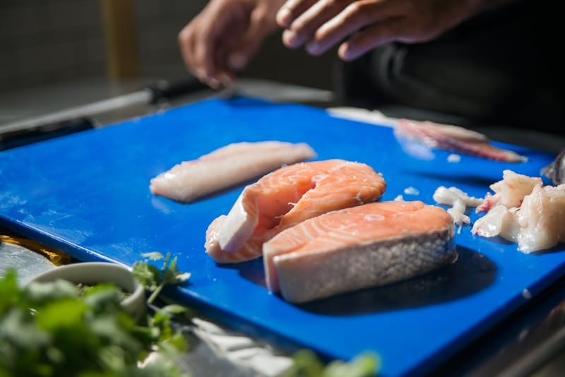 Close-up of salmon slices on a chopping board in a professional kitchen setting.