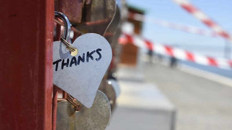 A heart-shaped love lock with 'THANKS' inscribed, hanging on a fence, symbolizing gratitude.