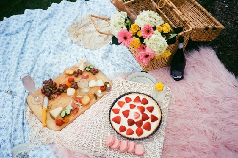 A delightful picnic scene with fresh food, flowers, and wine on a cozy outdoor setting.