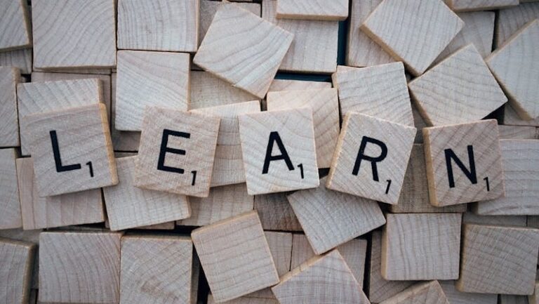 Wooden letter tiles arranged to spell 'learn' on a background of scattered tiles.