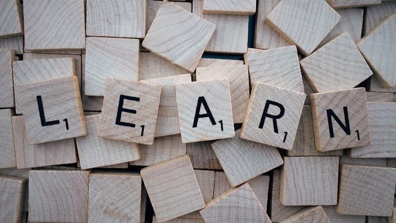 Wooden letter tiles arranged to spell 'learn' on a background of scattered tiles.