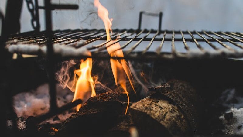 Close-up view of firewood burning in a fire pit with a metal grill above, outdoor setting.