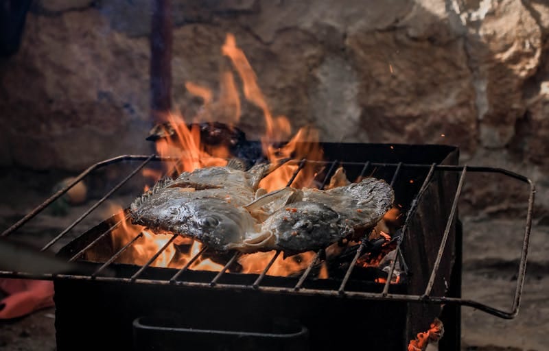 A grilled fish cooking over an open flame, showcasing traditional barbecue style.