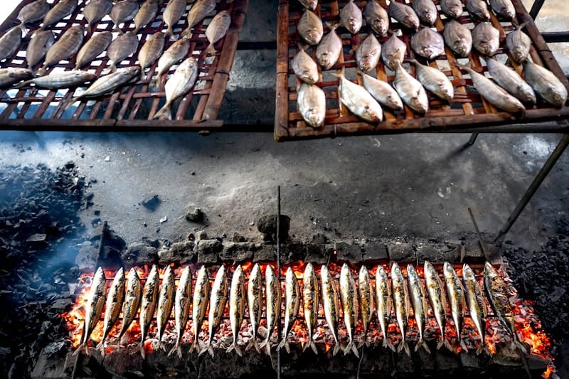 Traditional preparation of fresh fish grilling over an open flame, showcasing street food techniques.