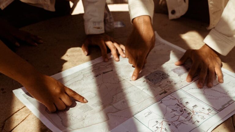 Group of hands pointing at a detailed map, planning an adventure trip in sunlight.