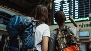 Two backpackers checking the digital board at a train station for travel information.